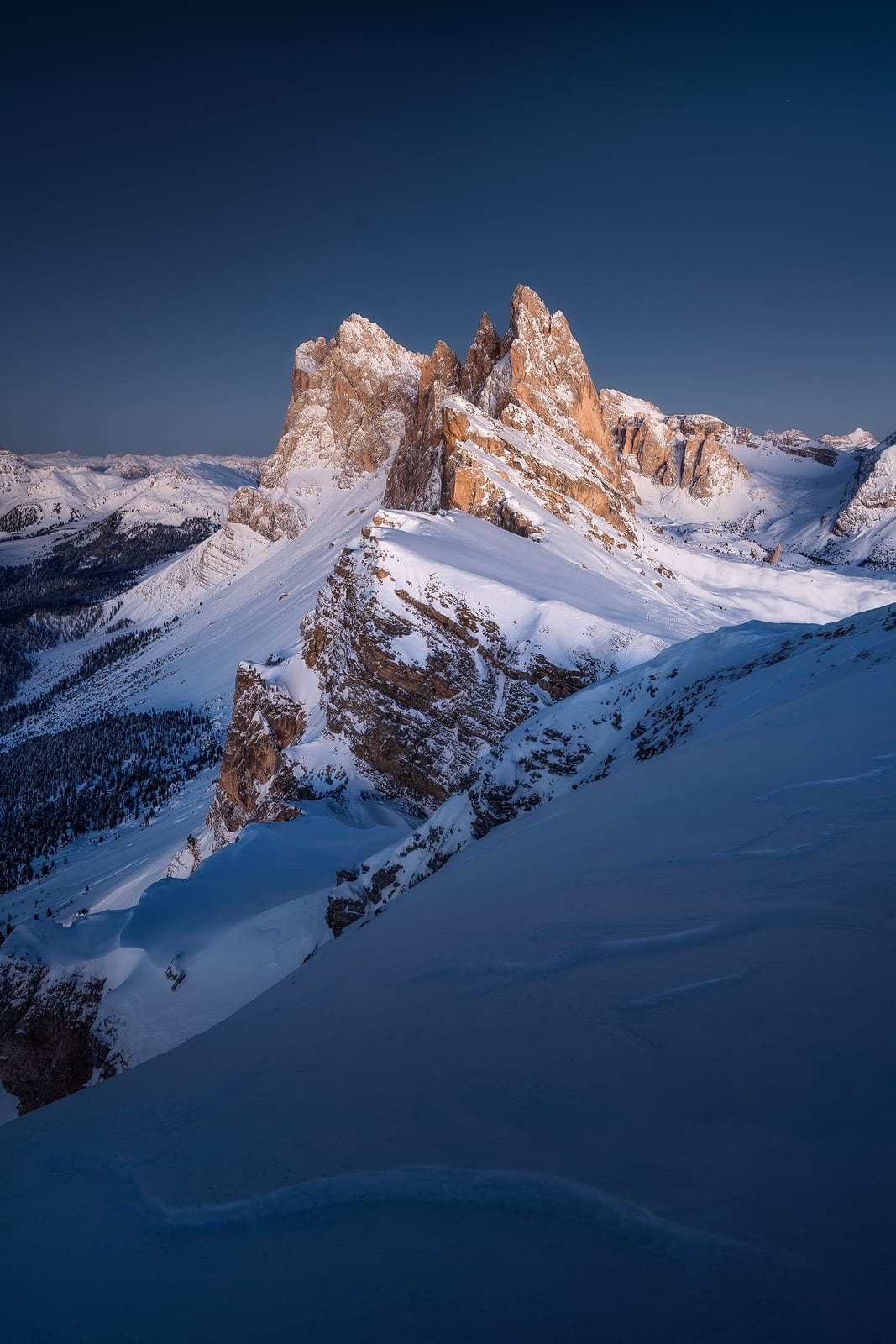 Snow-covered slopes rising to jagged peaks lit pink under a deep blue sky