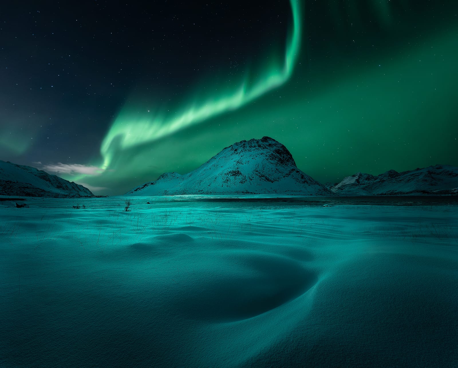 A green aurora arching over a snowy peak and a wind-carved snowfield