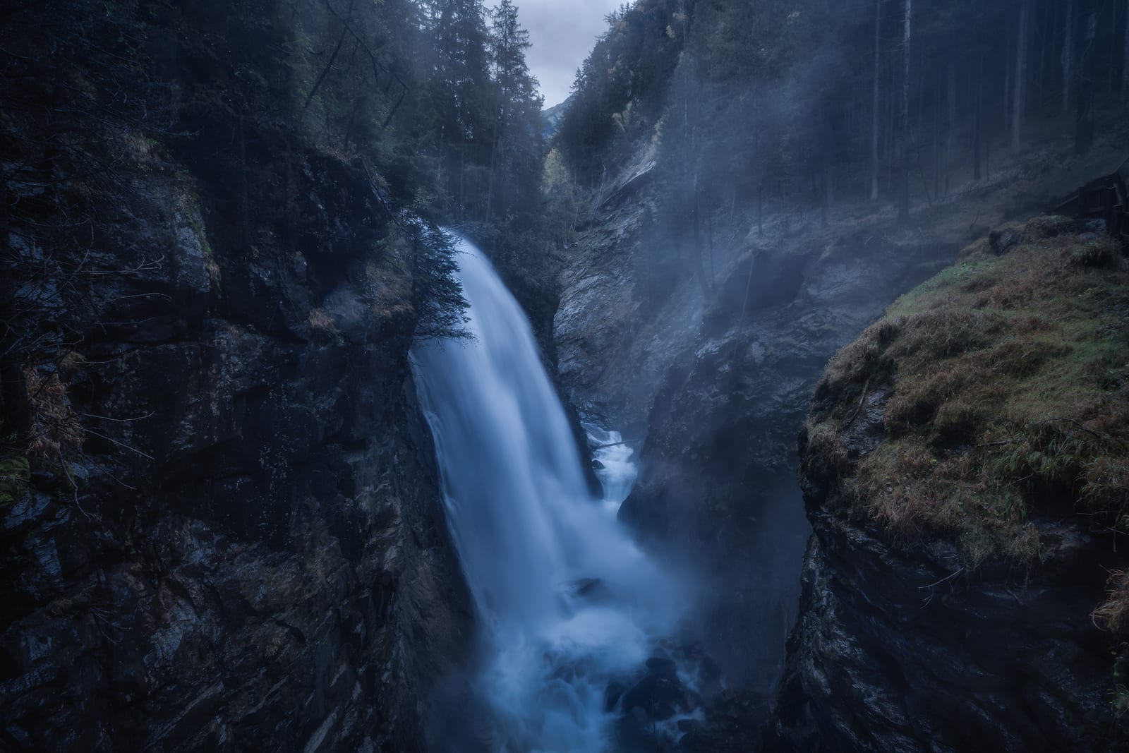 A waterfall plunging into a misty forest gorge