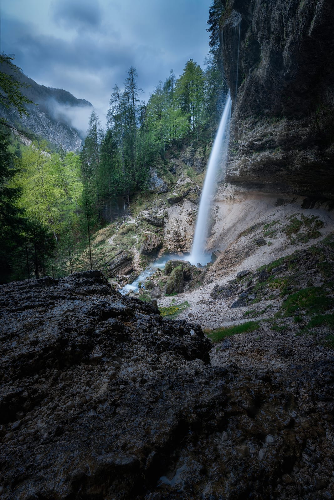 A slender waterfall dropping from a cliff into a green forested valley