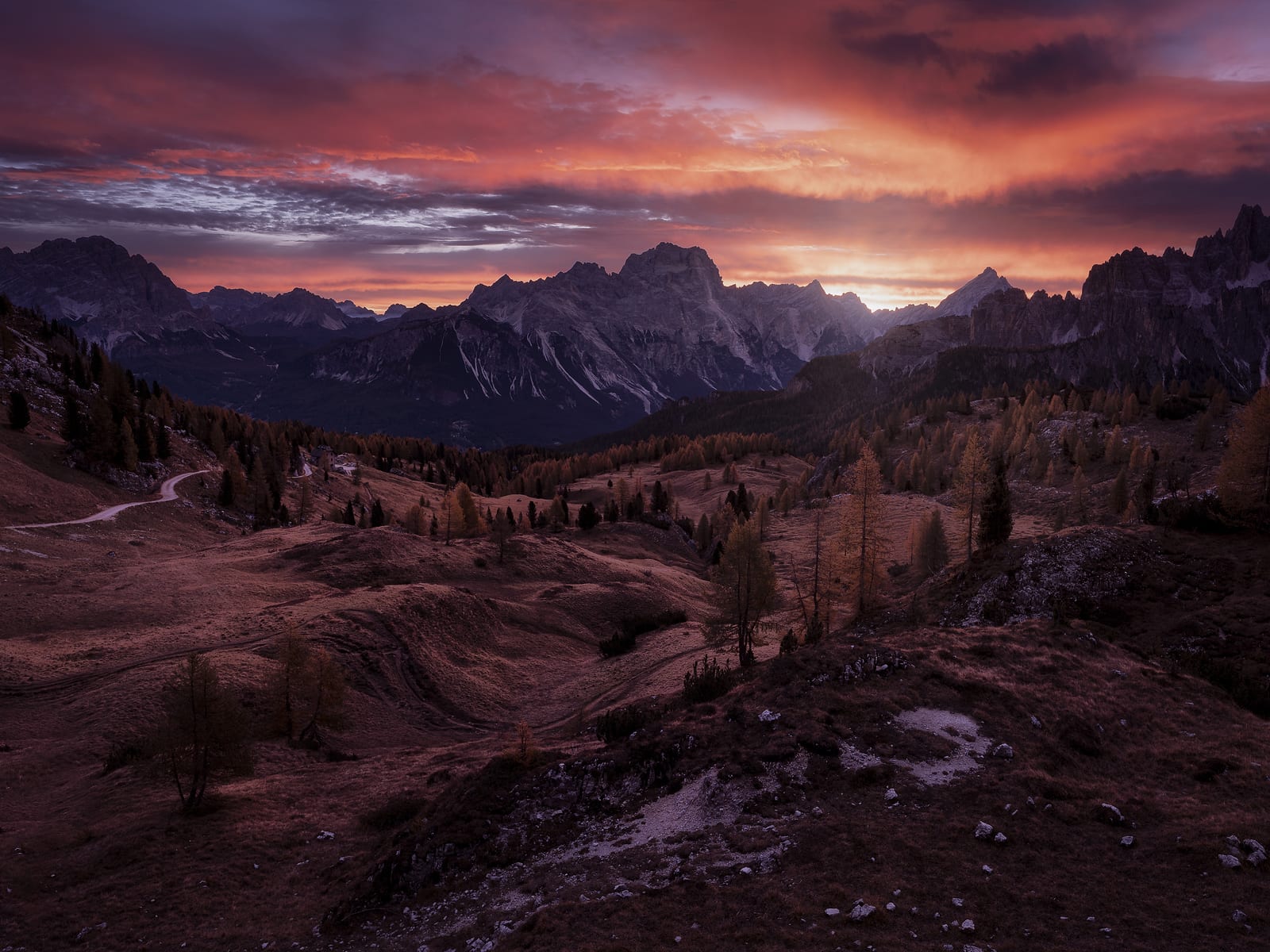 Larch meadows and a winding road below a red sky over the mountains