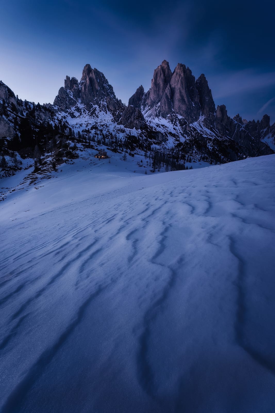 Wind-carved snow leading to a row of jagged peaks in blue light