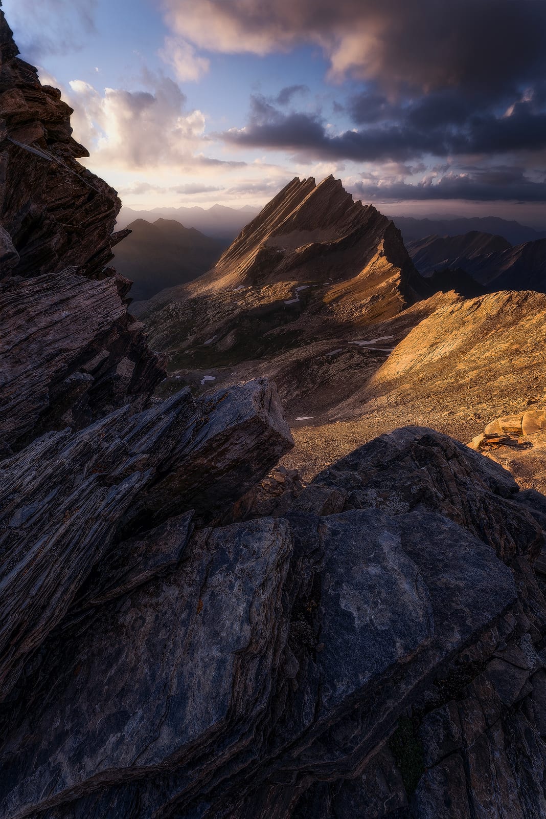 Sharp layered rock ridges glowing in late sun under a cloudy sky