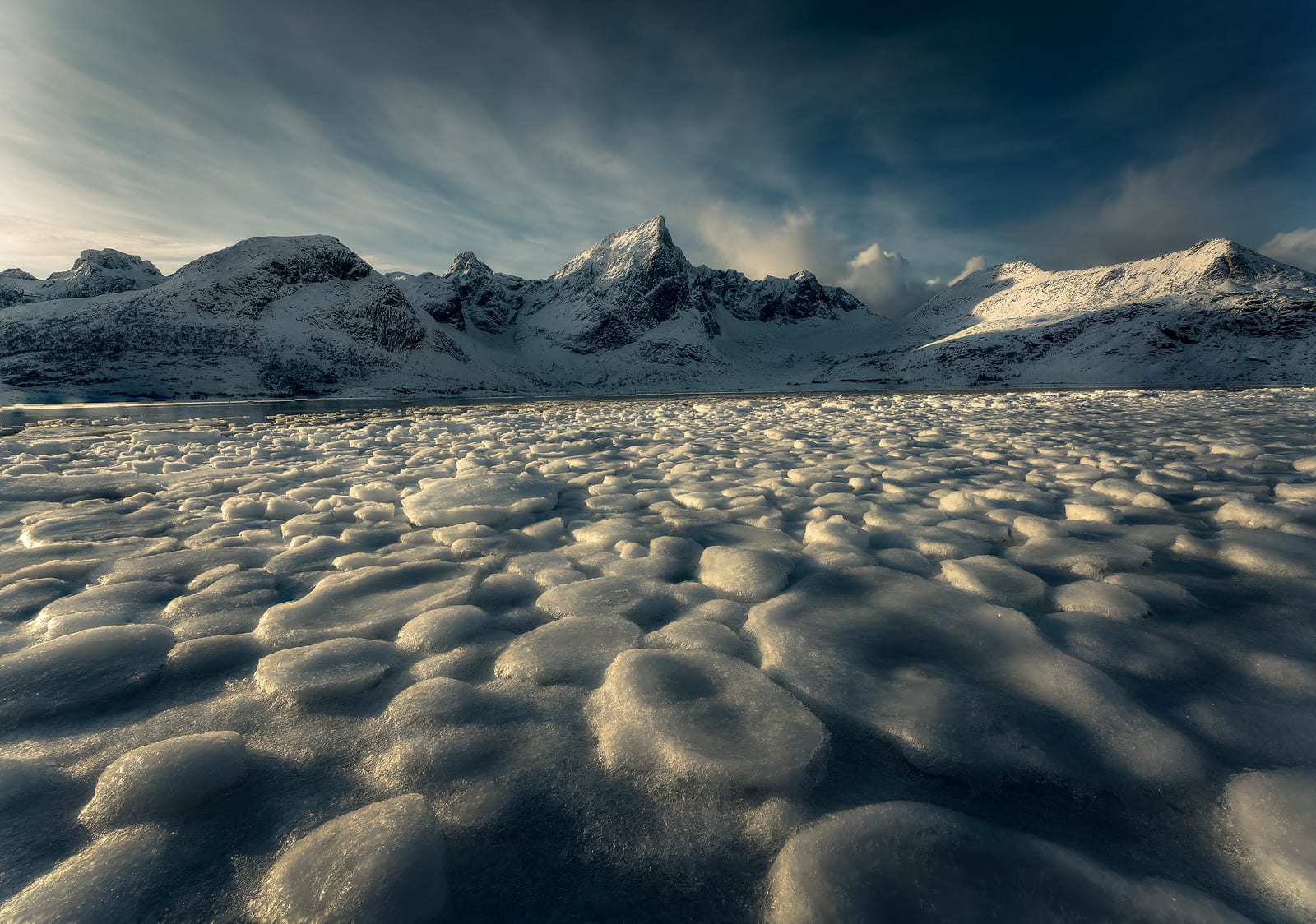 Discs of sea ice glowing in low sun below snowy peaks