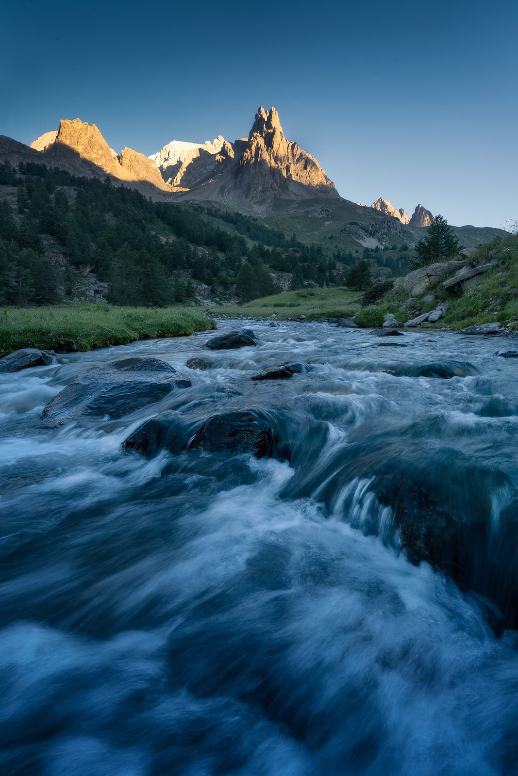 A fast mountain stream in the foreground and peaks lit by a low sun