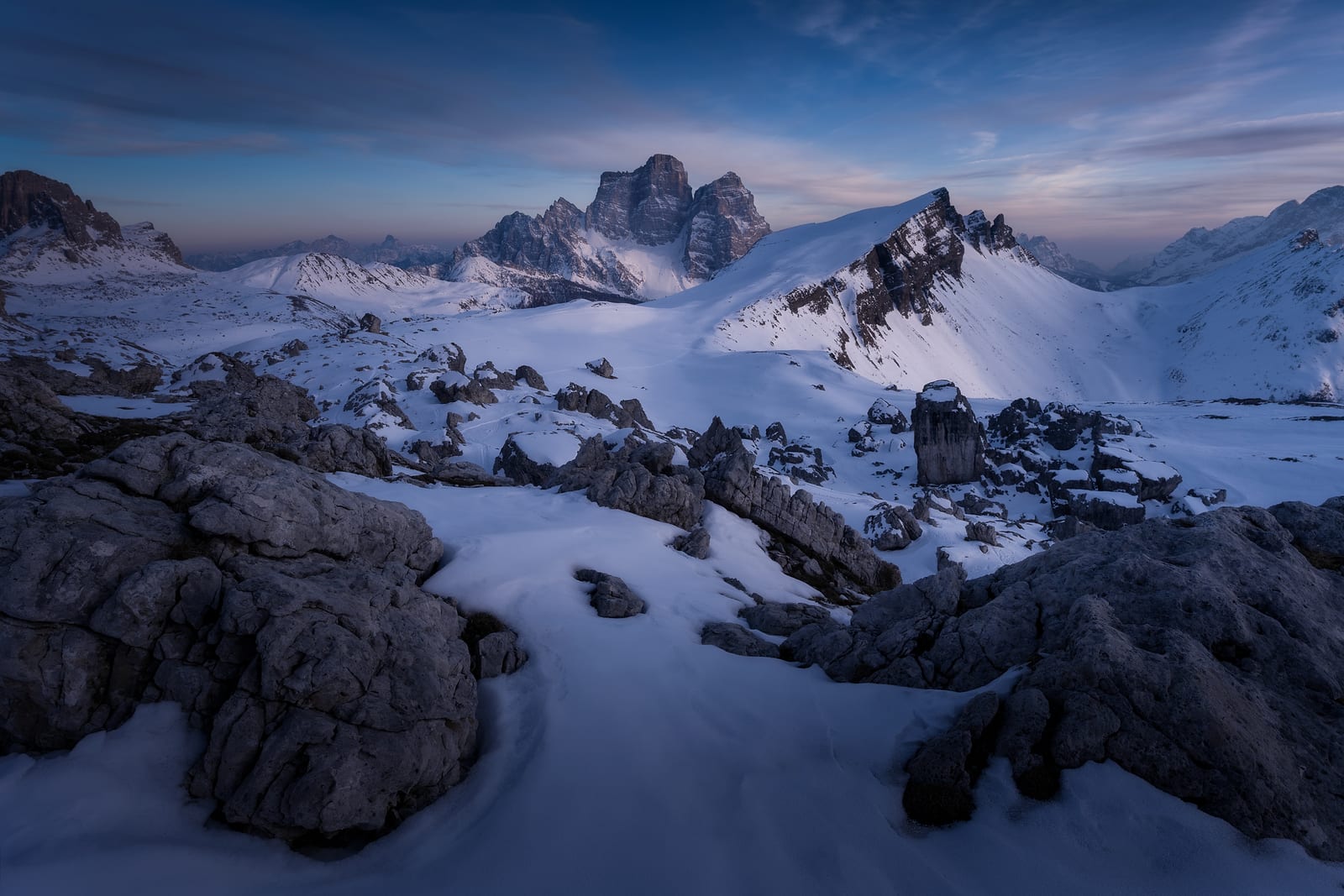 Snow and rocks below a massive rock peak at blue hour
