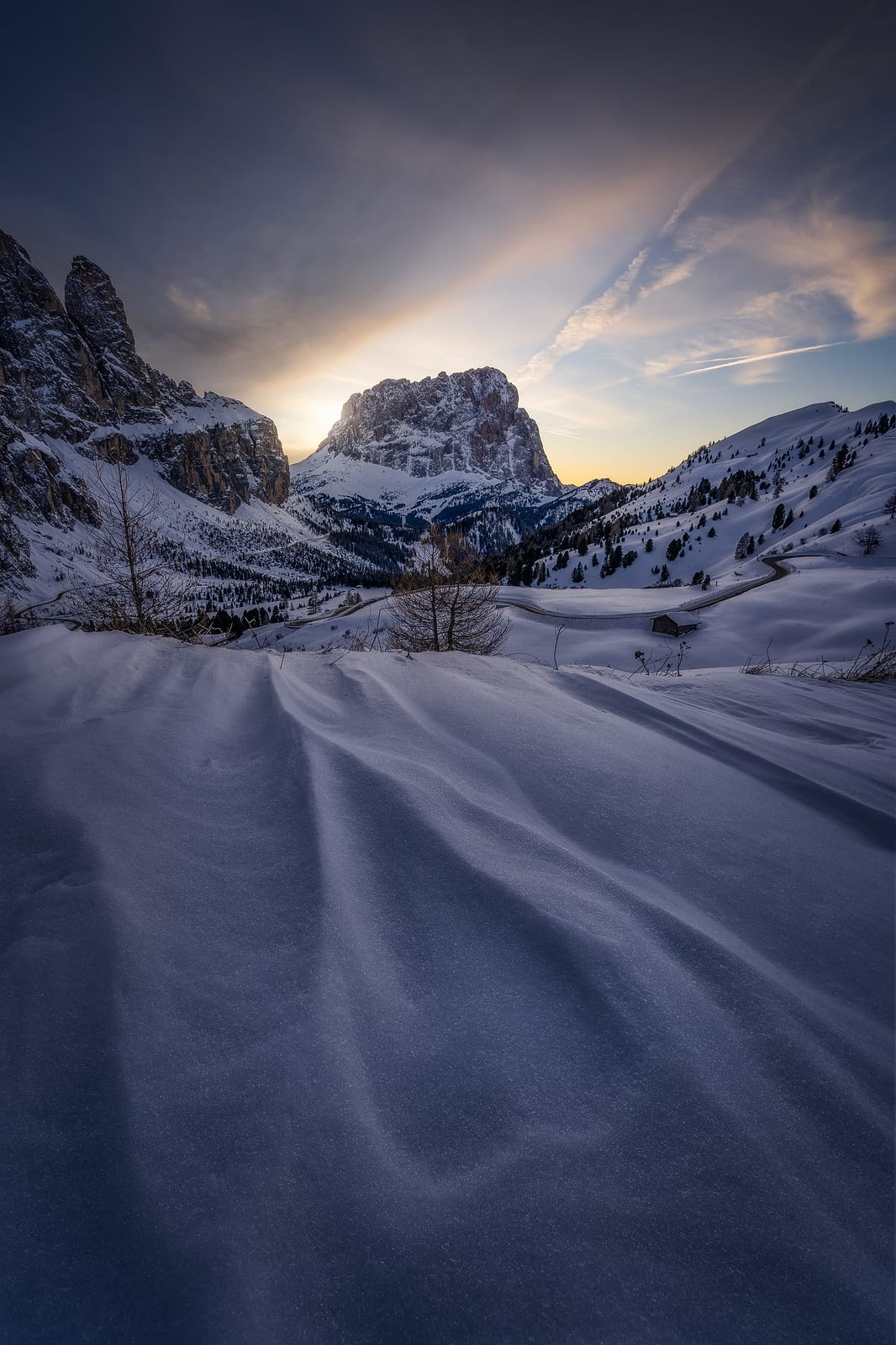 Rippled snow leading to snowy peaks with the sun setting behind them