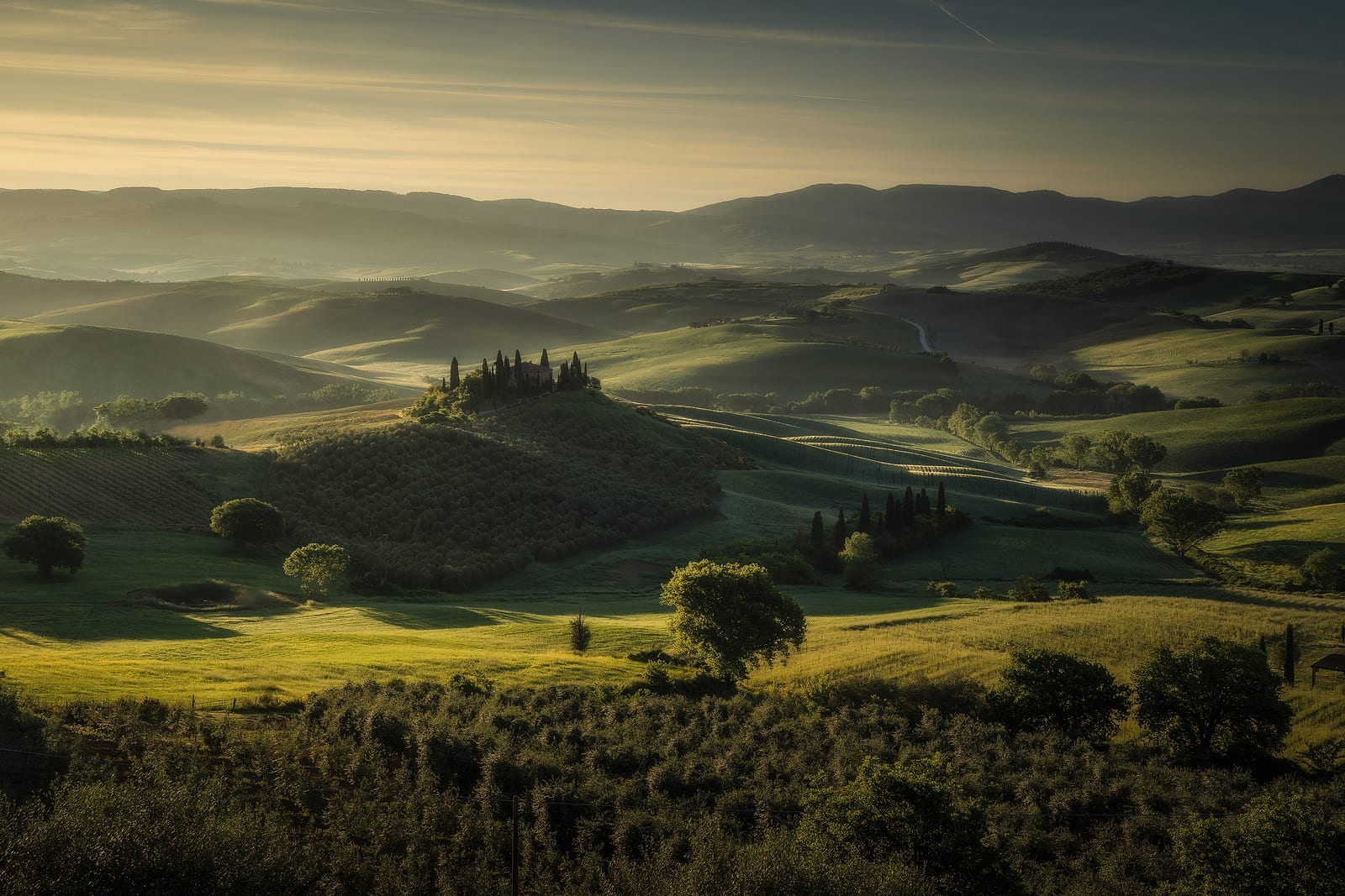 Rolling green hills with a lone farmhouse and trees in soft haze