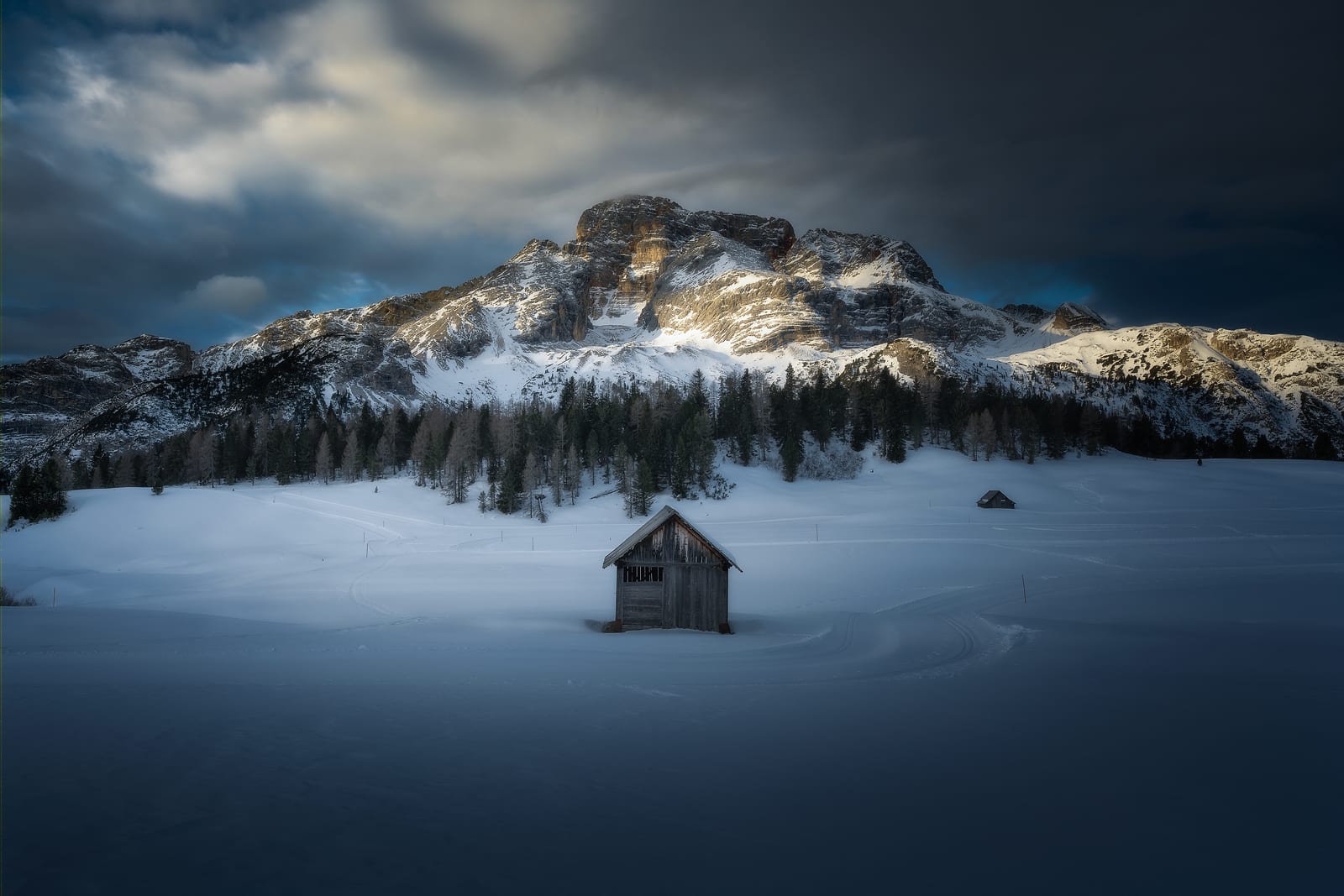 A lone wooden hut in a snowfield below a mountain catching the last sun