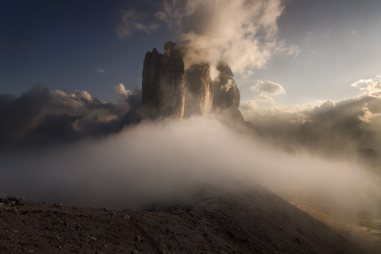 Three rock towers rising out of a sea of cloud in warm light