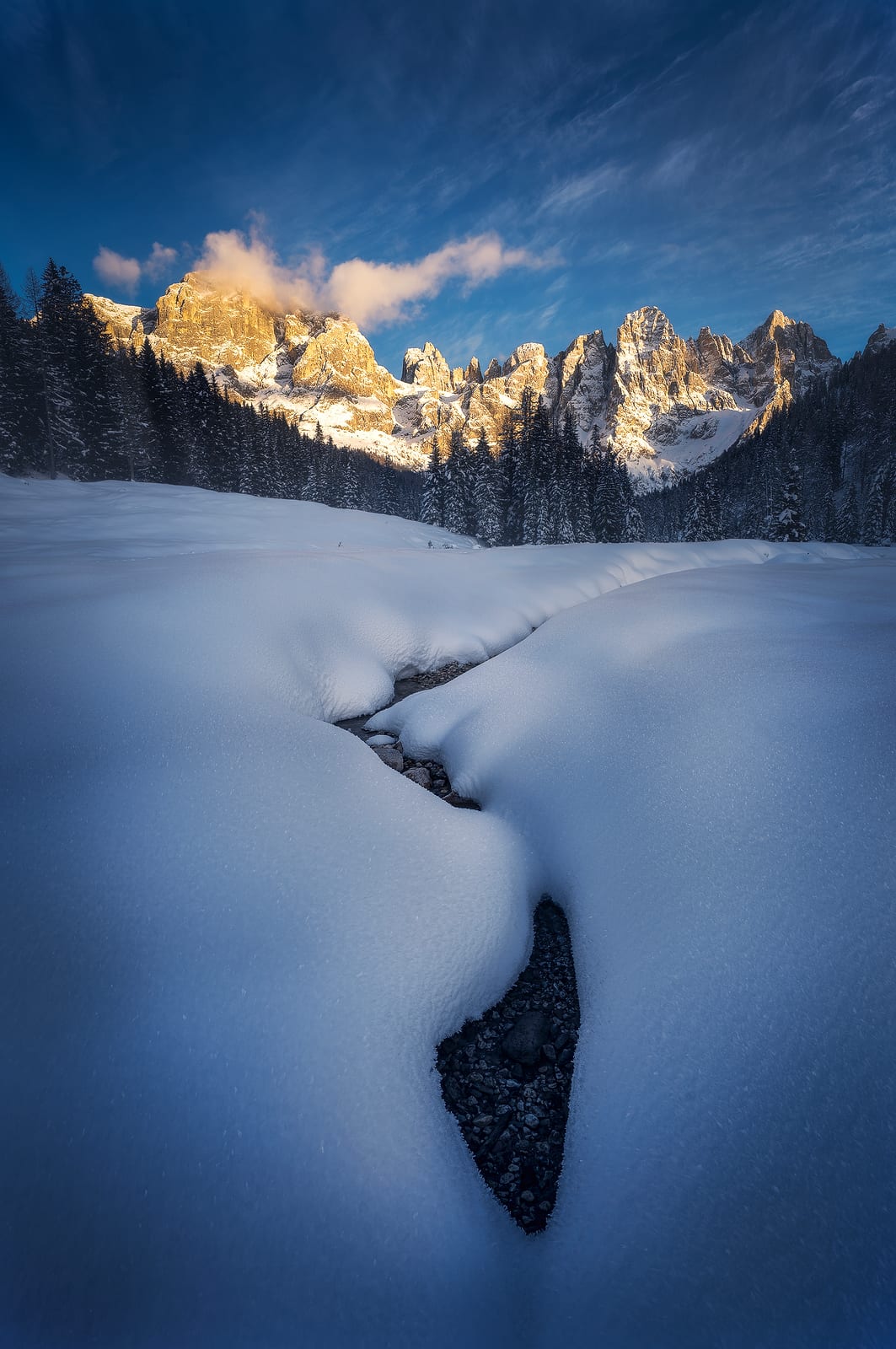 A stream cutting through deep snow toward peaks lit pink