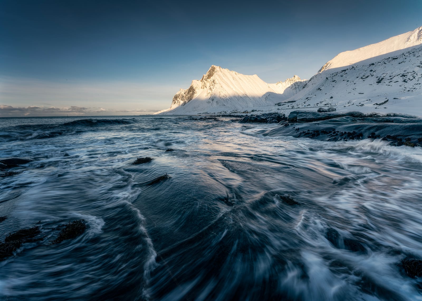 Long-exposure waves in the foreground and a snowy peak lit by low sun
