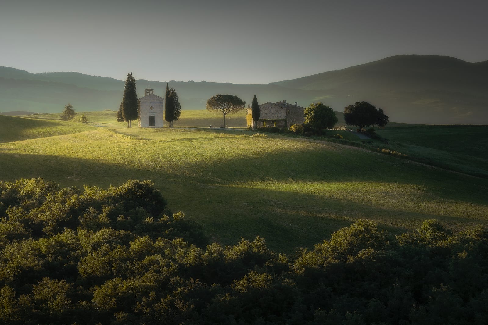 A small chapel between cypresses on a green hill in soft light